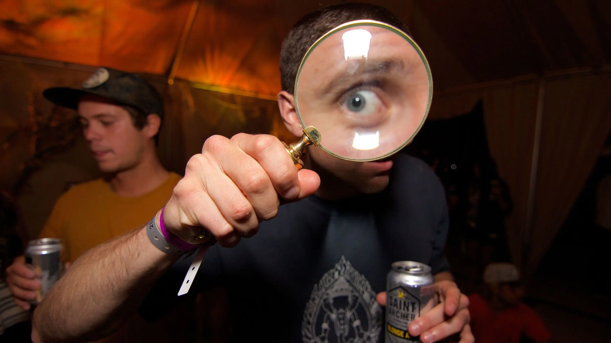 Man holding a magnifying glass up to his eye creating a visual representation of asking "Why?"